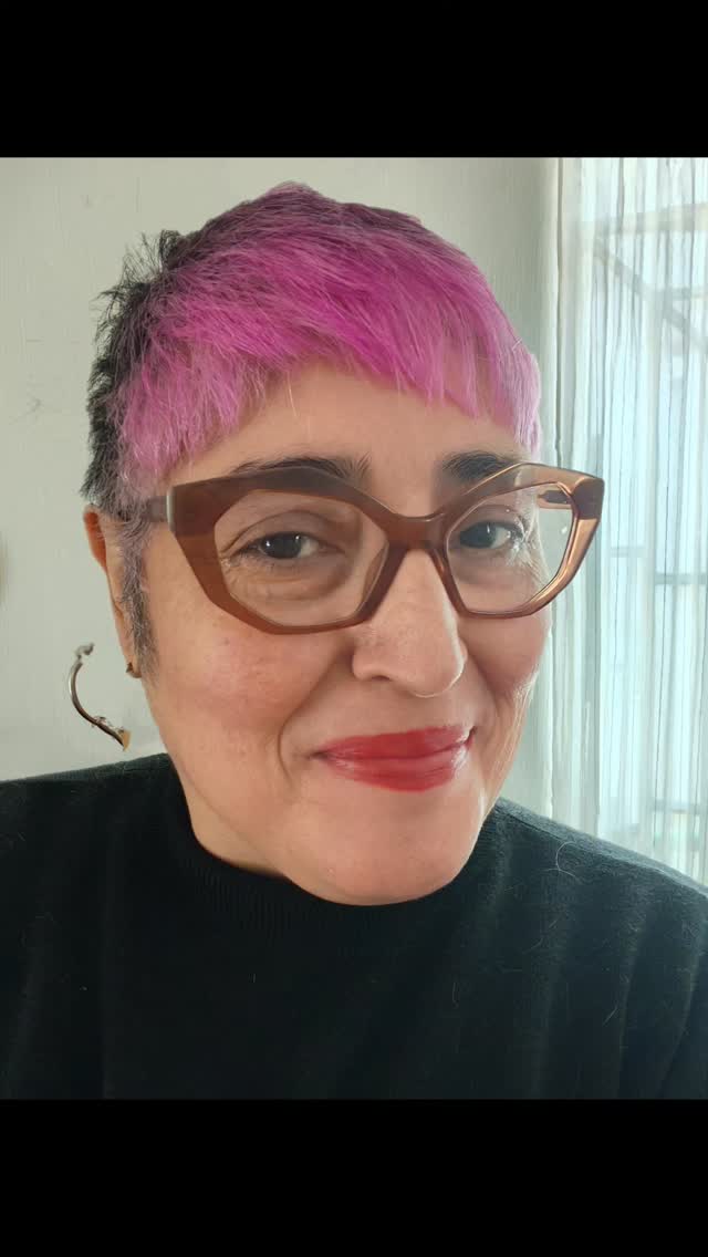 Martha Claudia Moreno con cabello rosa y gafas, retrato a color.